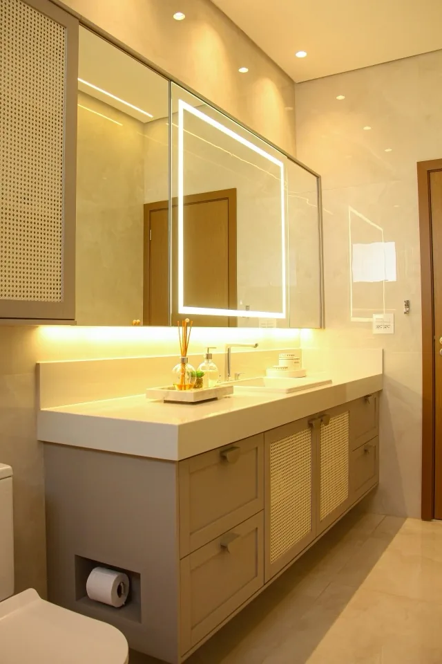 Banheiro planejado com portas em fibra natural trançada, bancada clara e espelho com iluminação embutida