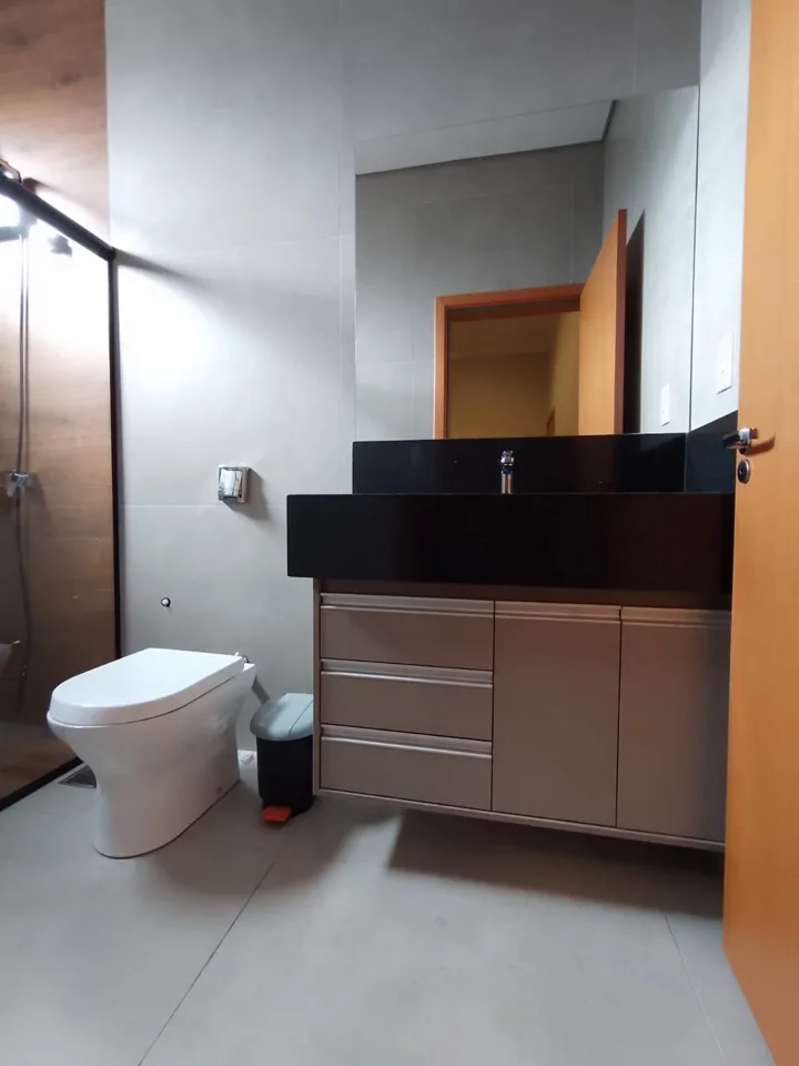 Banheiro planejado com bancada preta, cuba esculpida e armário em MDF claro ao lado do box de vidro