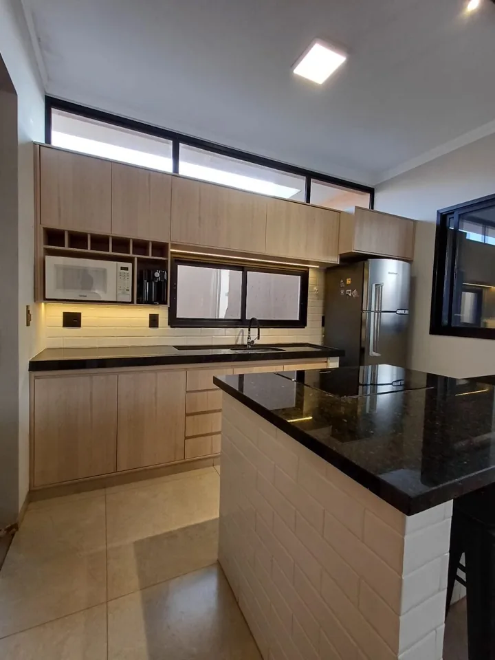 Cozinha com armários em madeira carvalho claro, península revestida de tijolinho e bancada de granito preto com cooktop