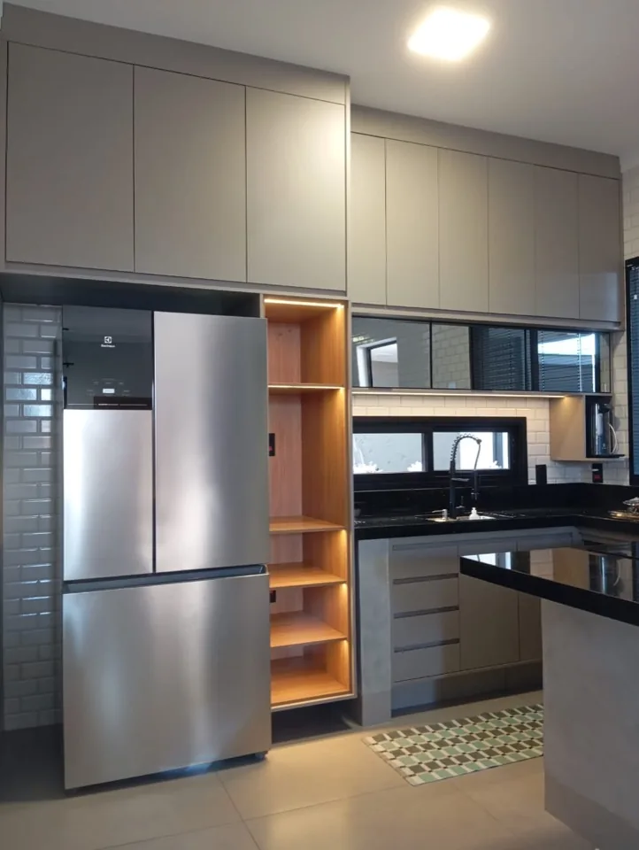 Cozinha em MDF fendi com geladeira french door inox, nicho vertical de madeira iluminado e revestimento de tijolinho branco