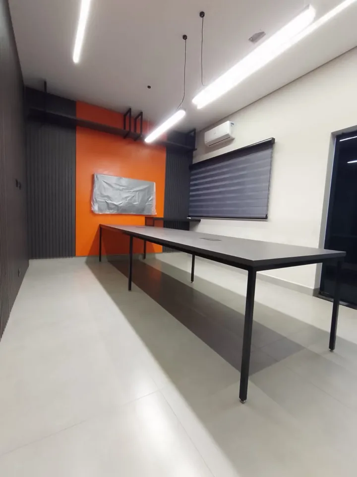 Sala de reunião planejada com mesa preta longa e parede laranja de destaque