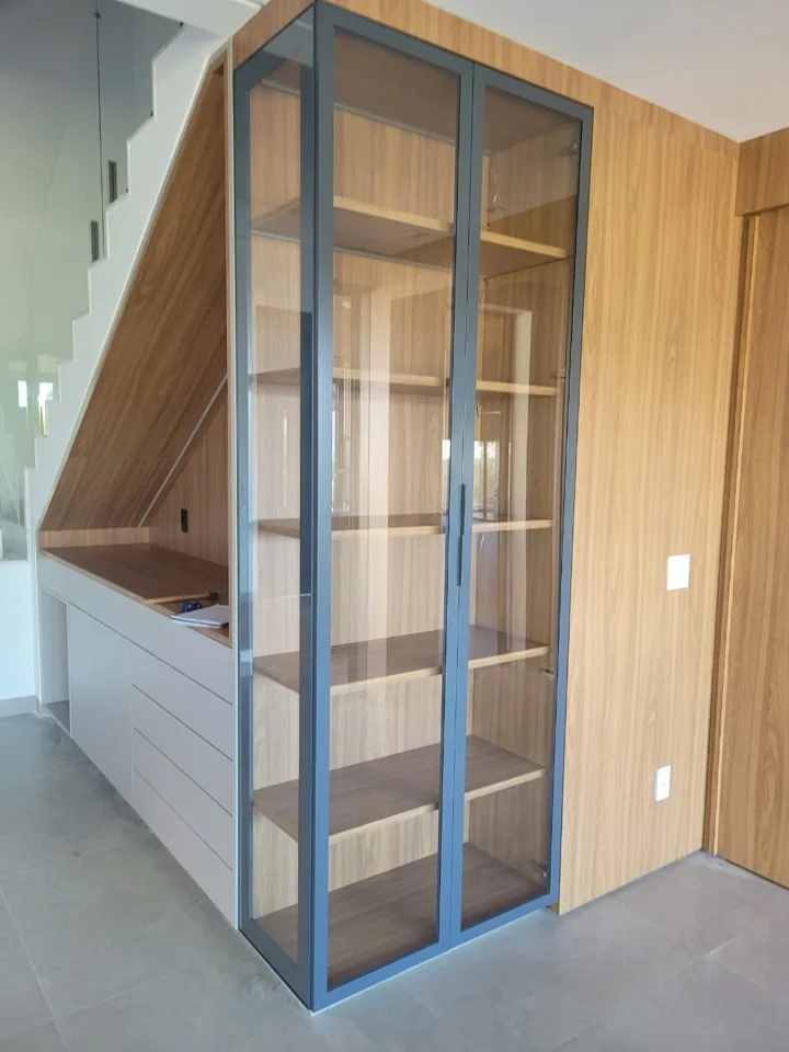Cristaleira planejada sob escada com portas de vidro fechadas e estrutura em metal grafite